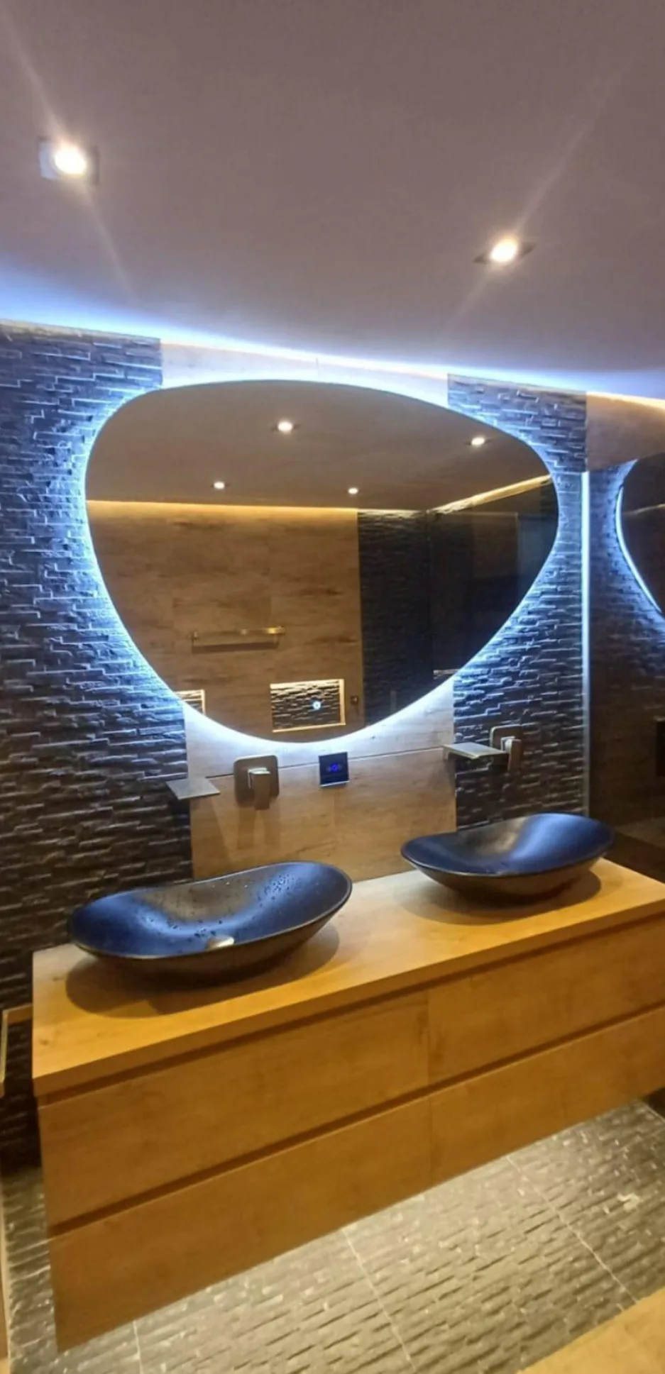 Badkamer met verlichte spiegel, houten wastafelmeubel en twee opzetwaskommen