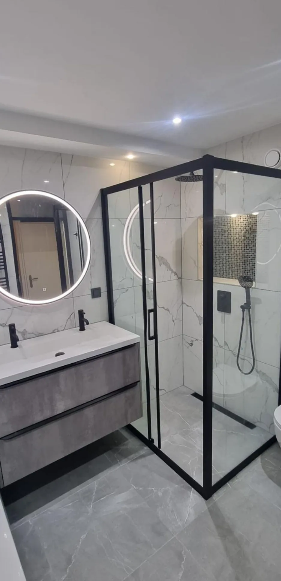 Badkamer met marmerlook tegels, ronde ledspiegel en inloopdouche met zwart kader