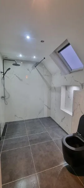 Badkamer onder een schuin dak met dakraam, marmerlook tegels, zwarte regendouche en zwart hangtoilet