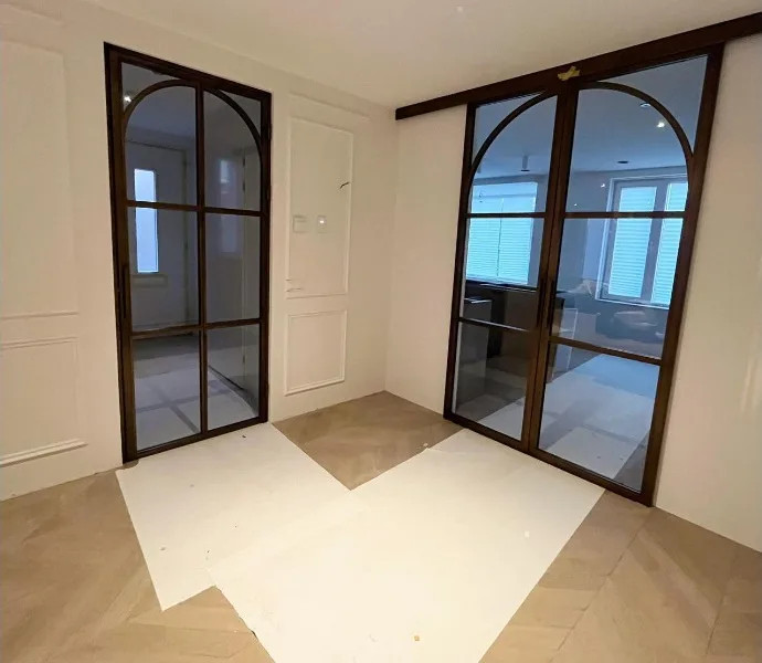 Twee stalen glasdeuren met boog, waarvan één schuifdeur, in een kamer met wandpanelen