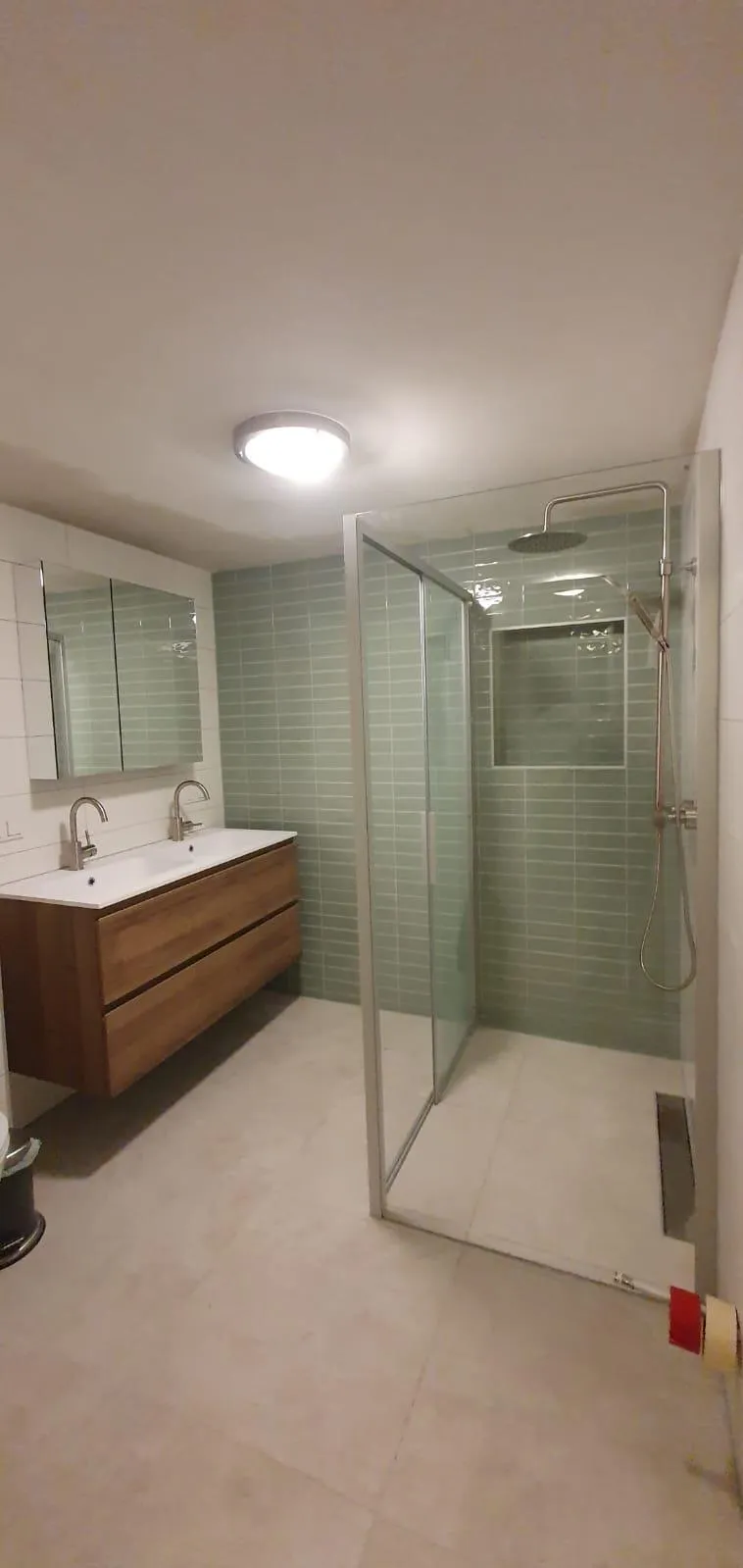Badkamer met groene wandtegels in de douche, glazen douchewand en houten wastafelmeubel