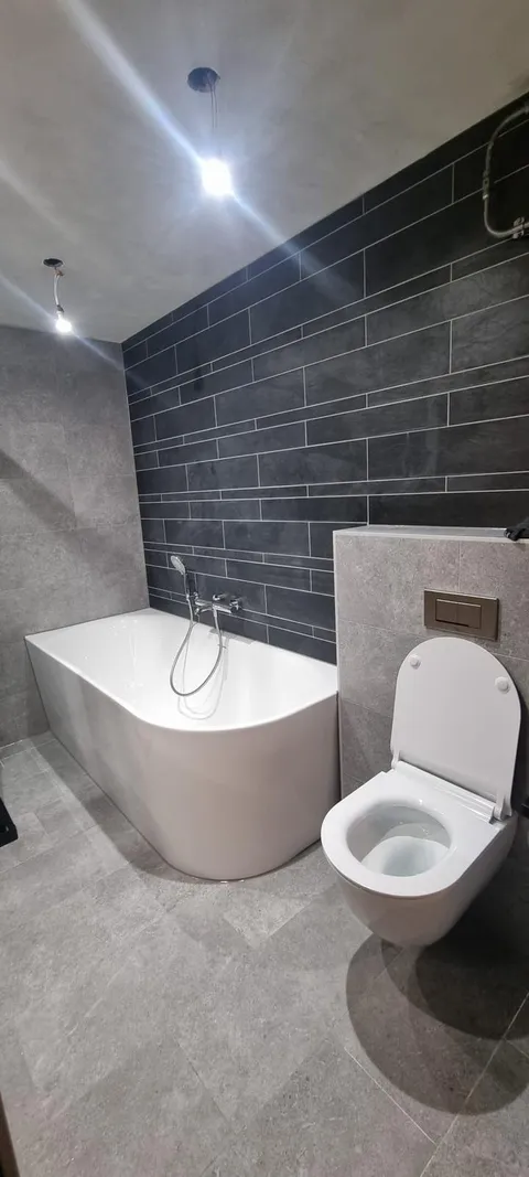 Badkamer met vrijstaand bad, hangtoilet en donkere tegelwand