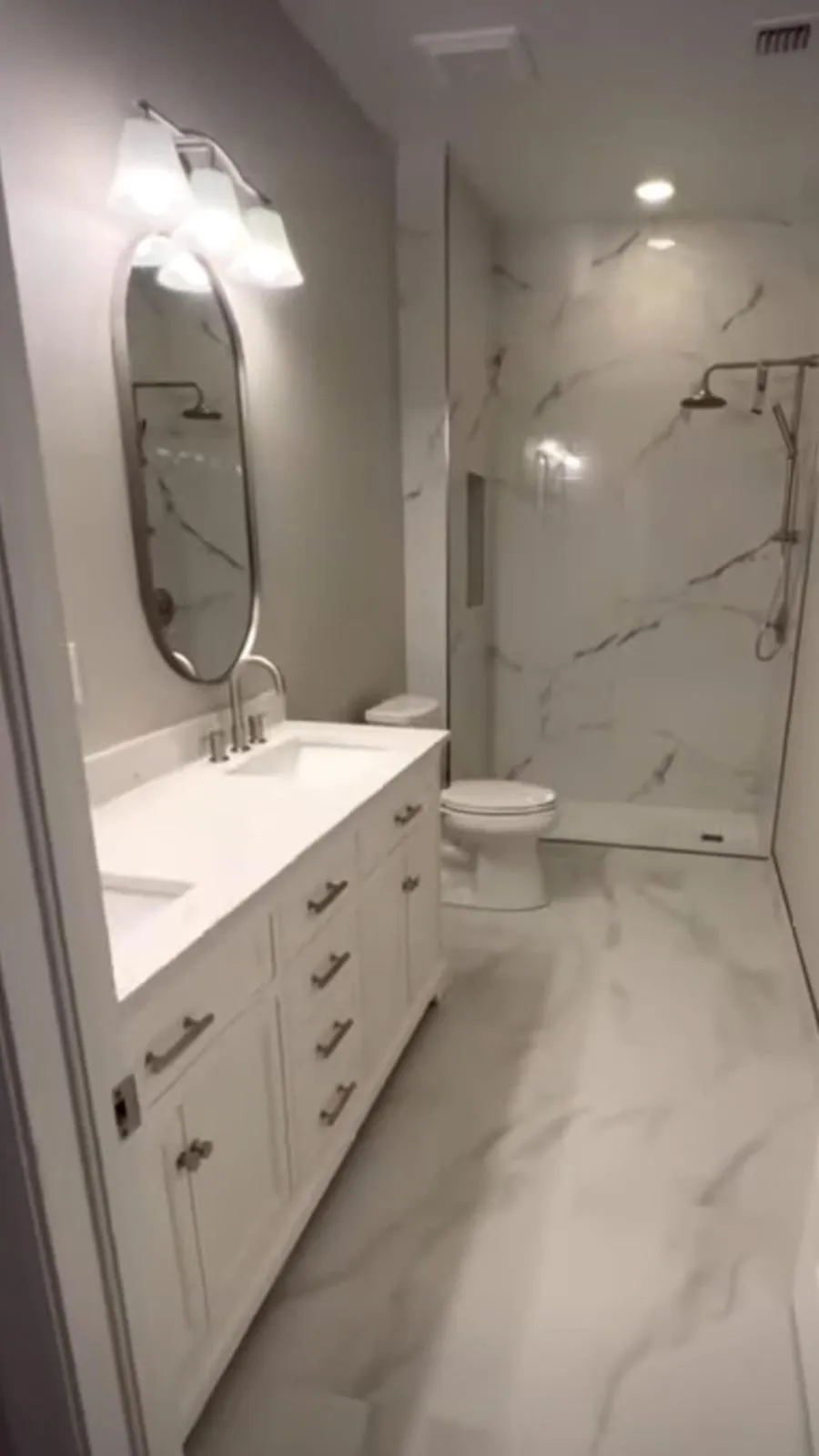 Badkamer in witte marmerlook met ovale spiegel, wit wastafelmeubel en inloopdouche