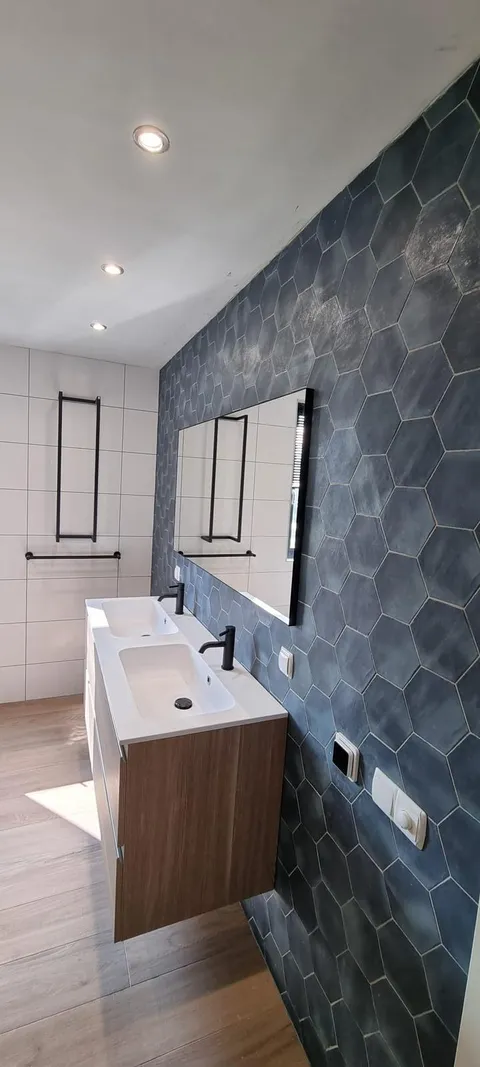 Badkamer met blauwe zeshoekige wandtegels, houten wastafelmeubel en zwarte kranen