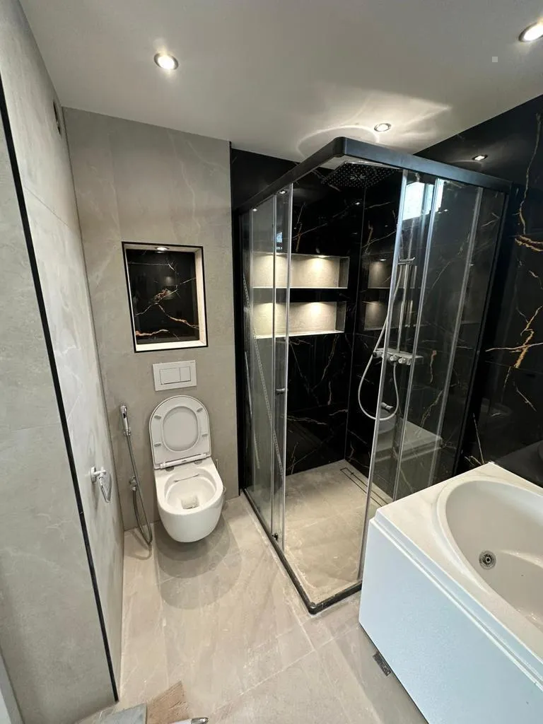 Badkamer met douchecabine in zwart marmerlook, verlichte nissen, hangtoilet en bad