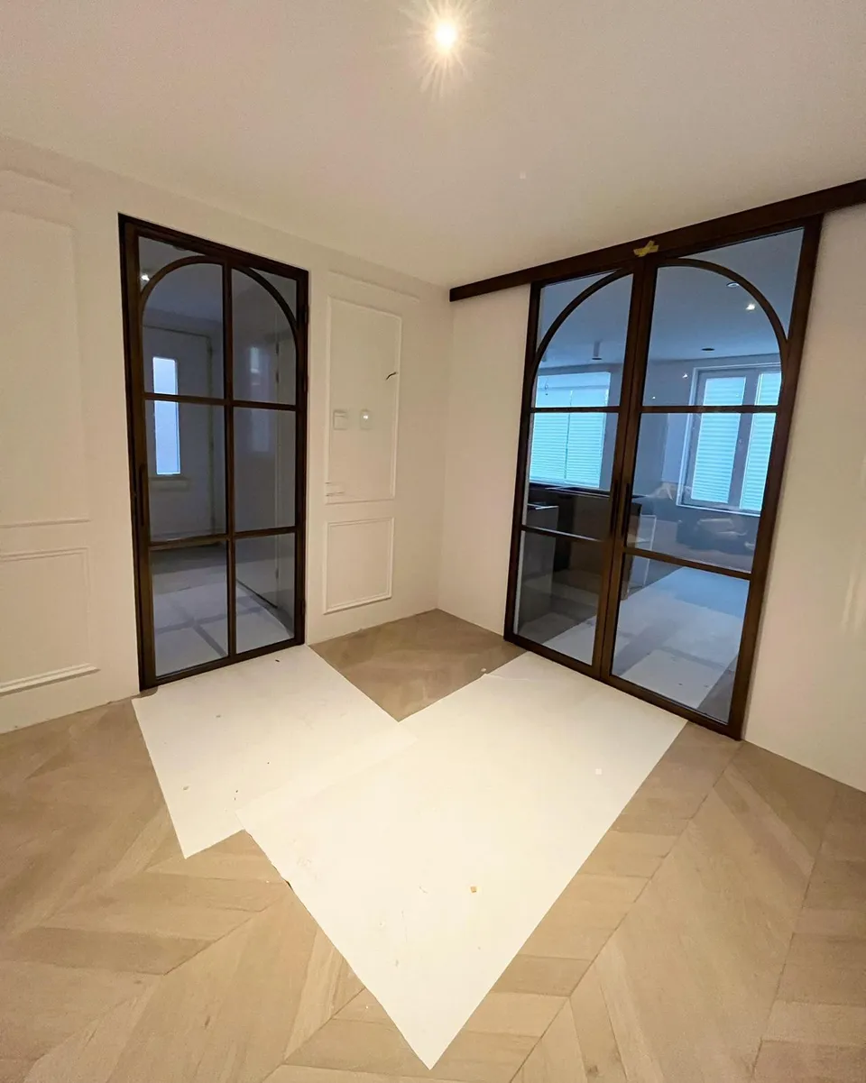 Twee stalen glasdeuren met boog, waarvan één schuifdeur, in een kamer met wandpanelen