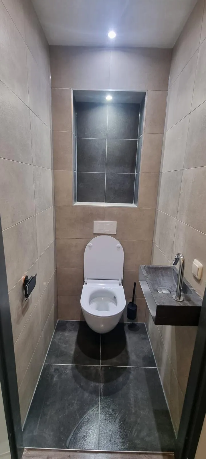 Hangend toilet tegen antraciet tegels met verlichte nis en fonteintje